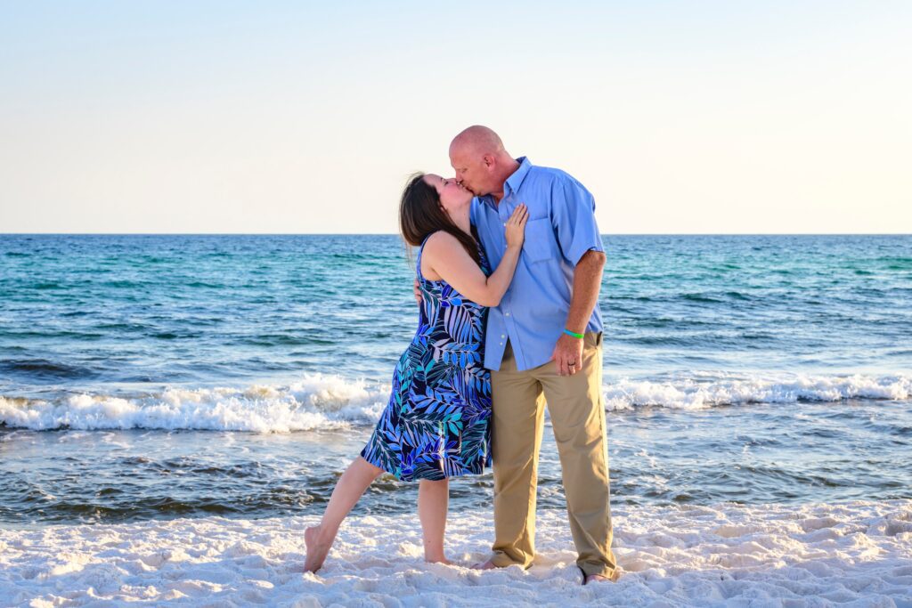 A man and woman kissing on the beach.