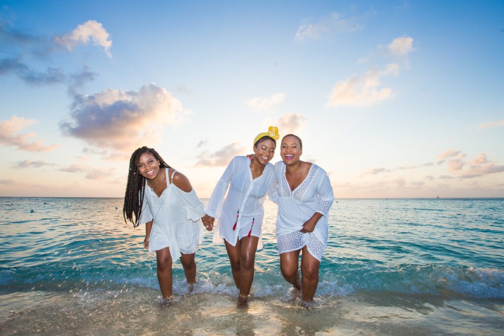 Three people in white clothes are standing on the beach.