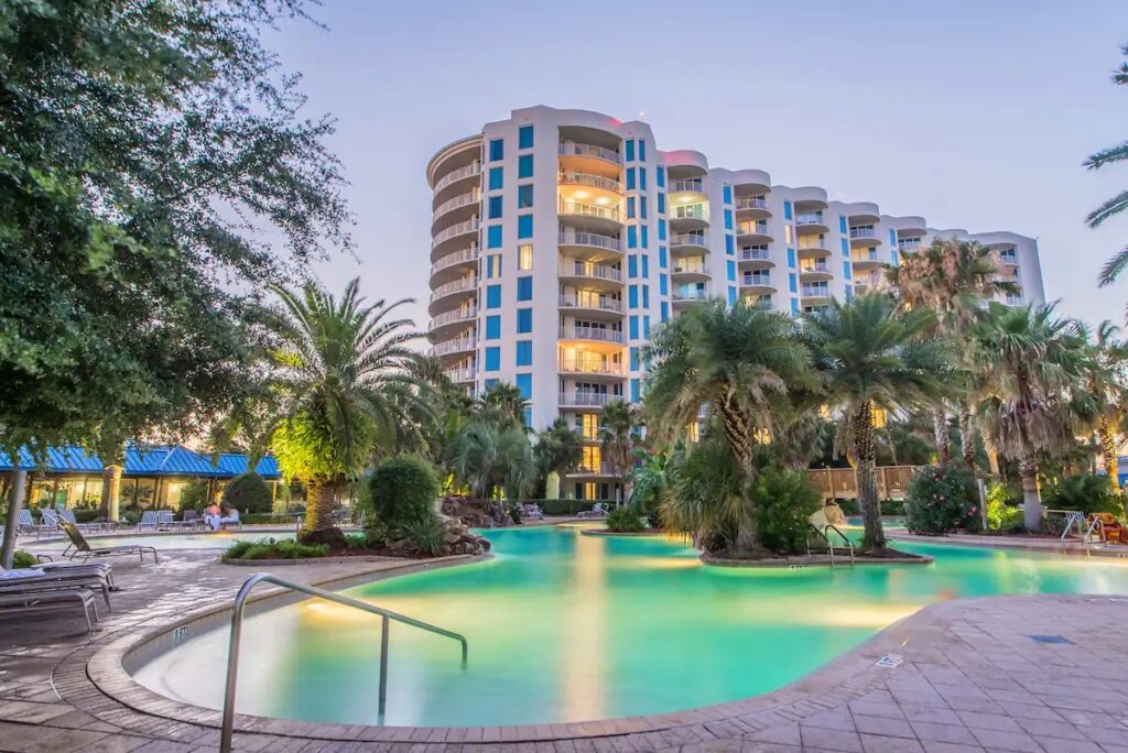 A pool with palm trees and a building in the background.