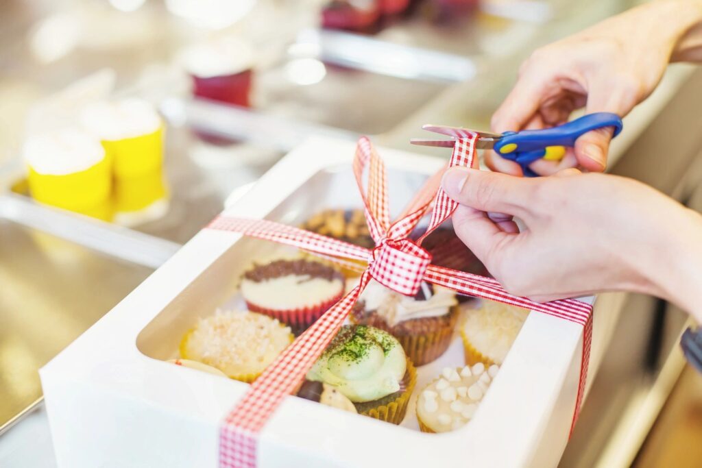 A person cutting cupcakes with scissors on top of the box.